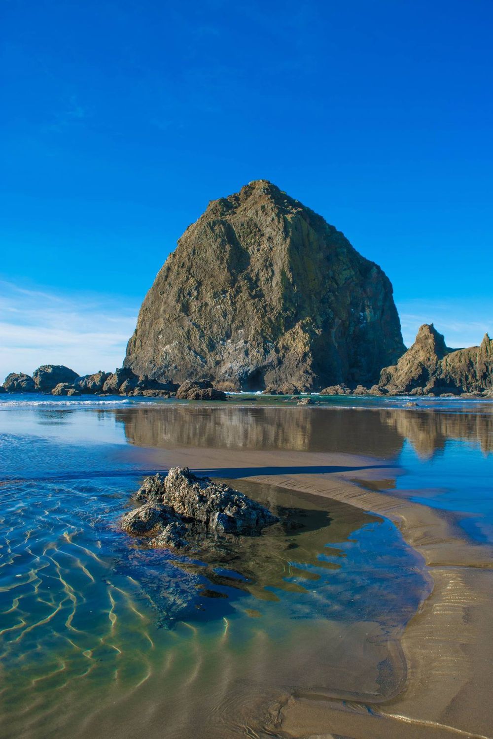 Haystack Rock stands majestically on Cannon Beach with tide pools reflecting in the foreground.
