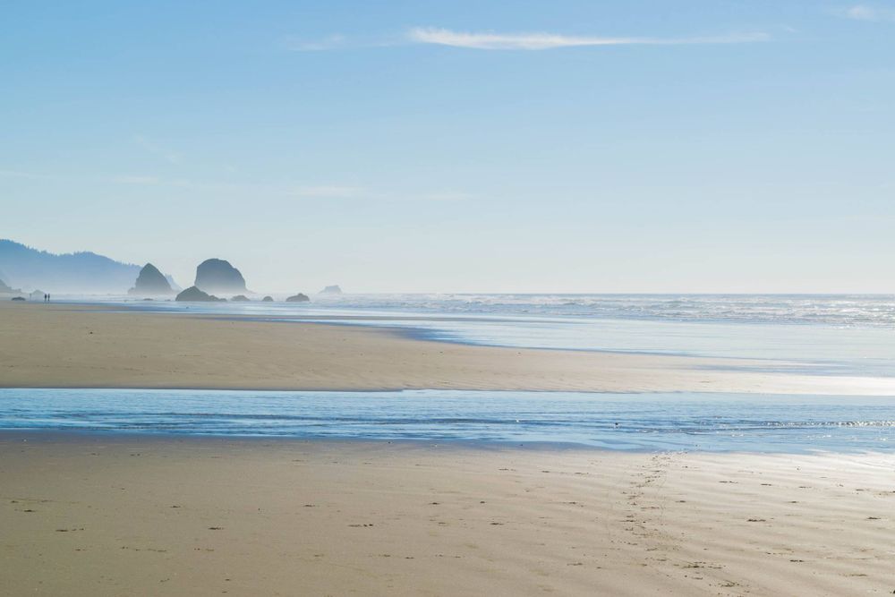 Serene beach landscape with distant sea stacks and mountains under clear blue skies.