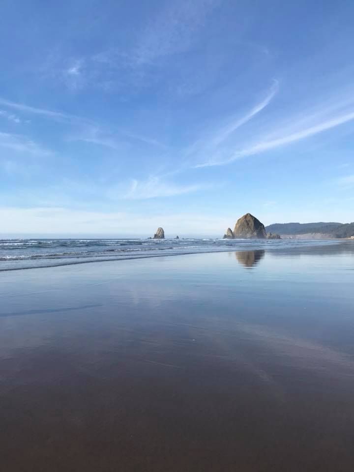 Haystack Rock reflects in wet sand during low tide at Cannon Beach, Oregon.