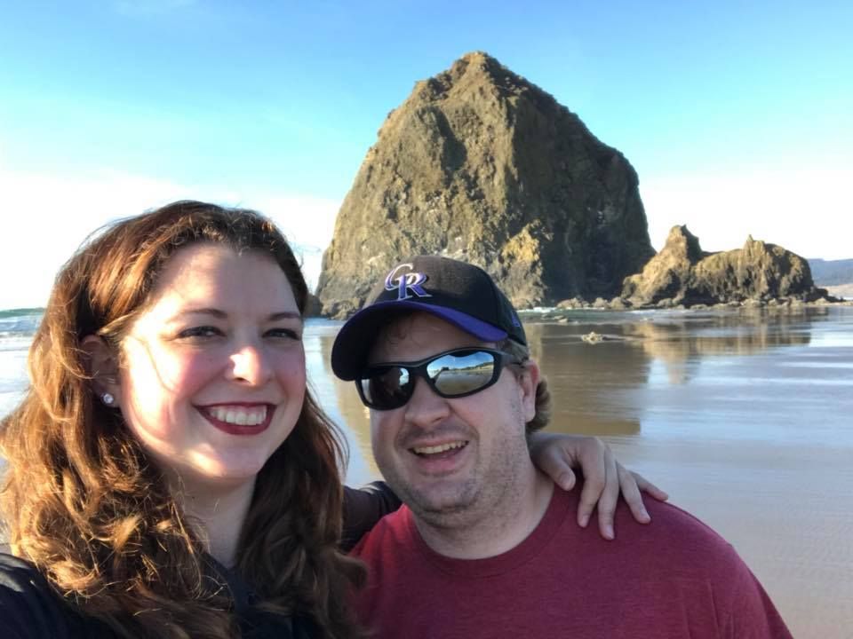 A rock formation looms behind beachgoers enjoying a sunny day at Cannon Beach.