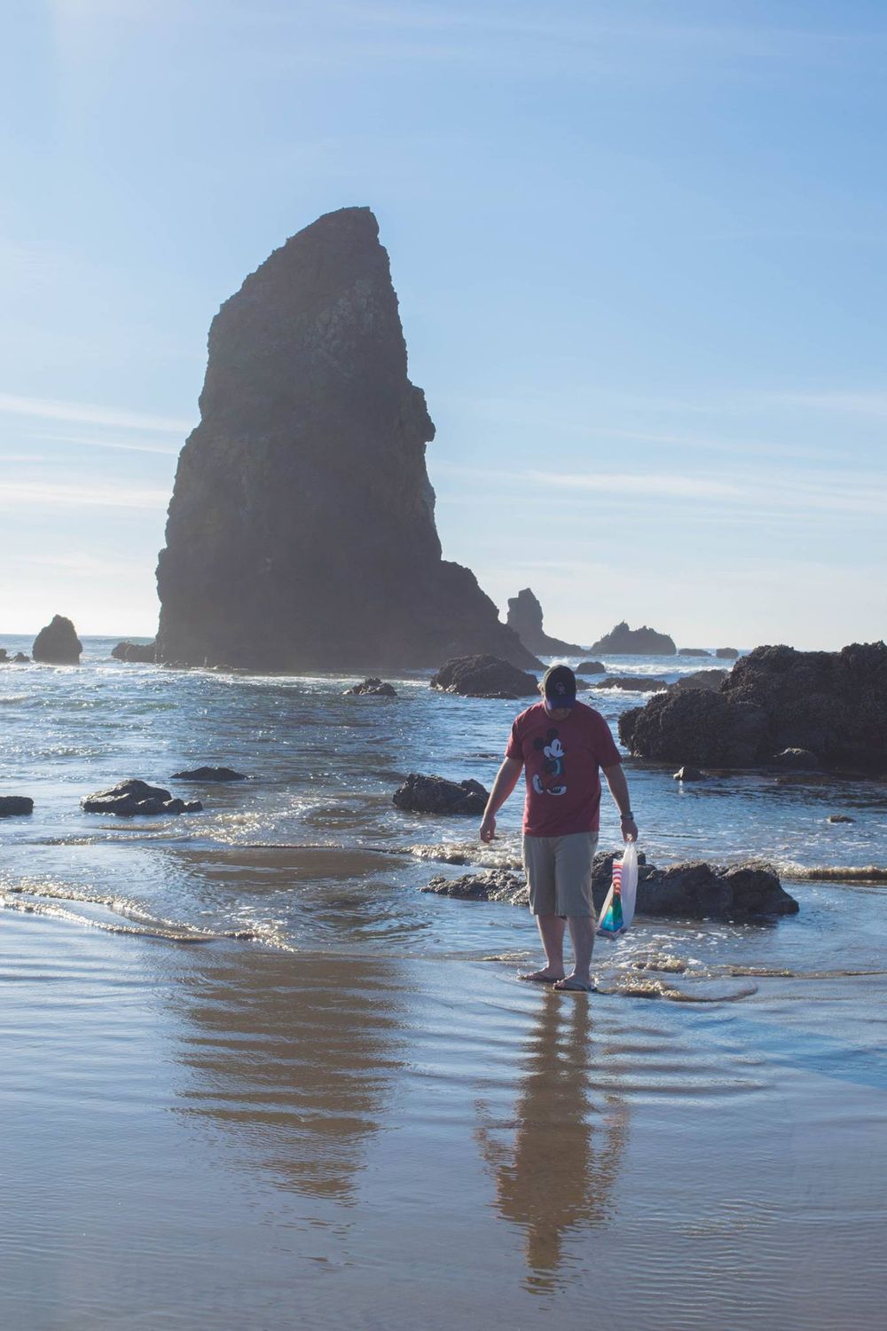Figure walks along the shoreline near a towering sea stack at Cannon Beach.