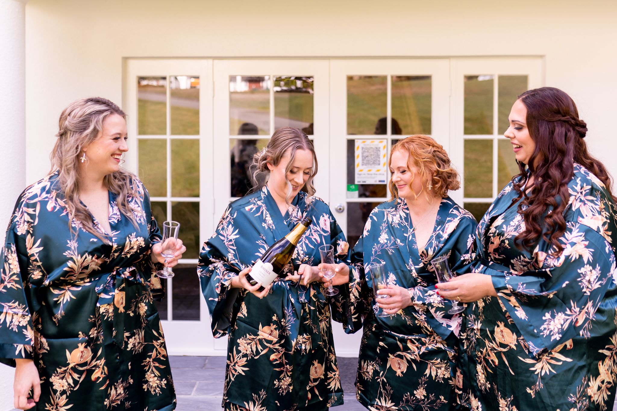 Group wearing matching floral robes sharing a joyful moment at a wedding venue.