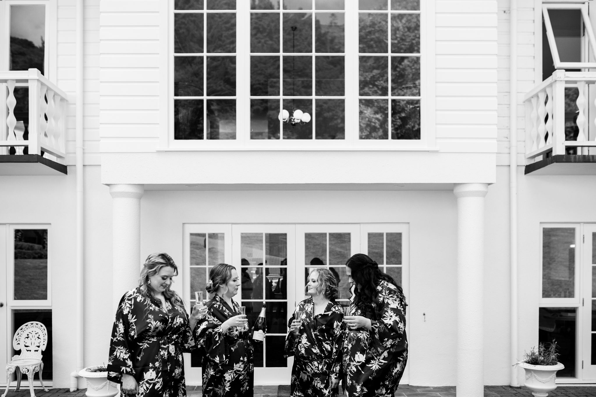 Black and white photo of group in matching floral robes standing outside white building.
