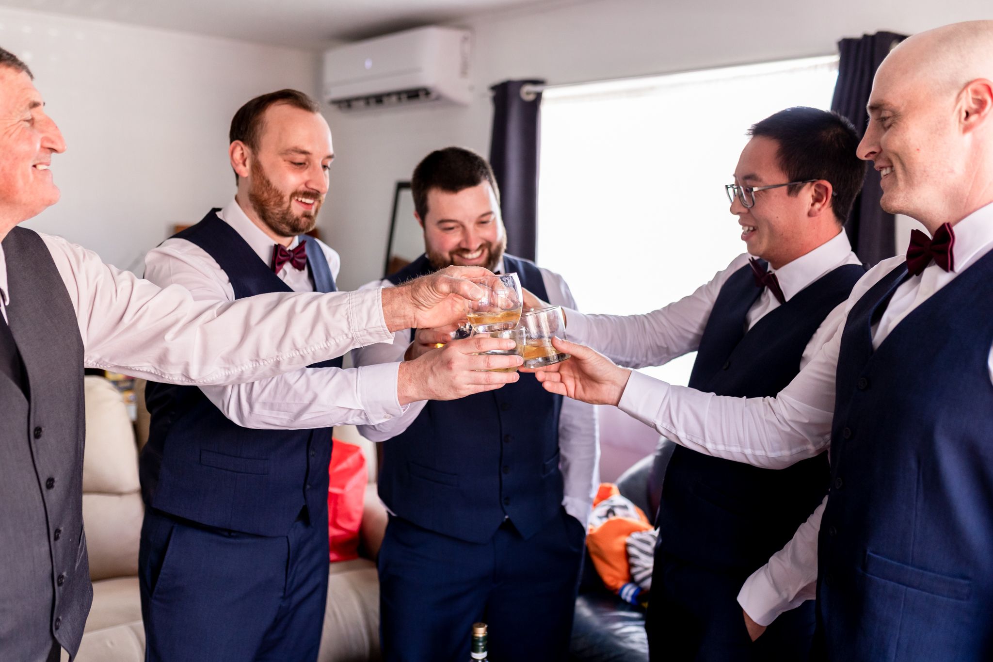 Groomsmen in formal attire toasting with drinks during pre-wedding celebration.