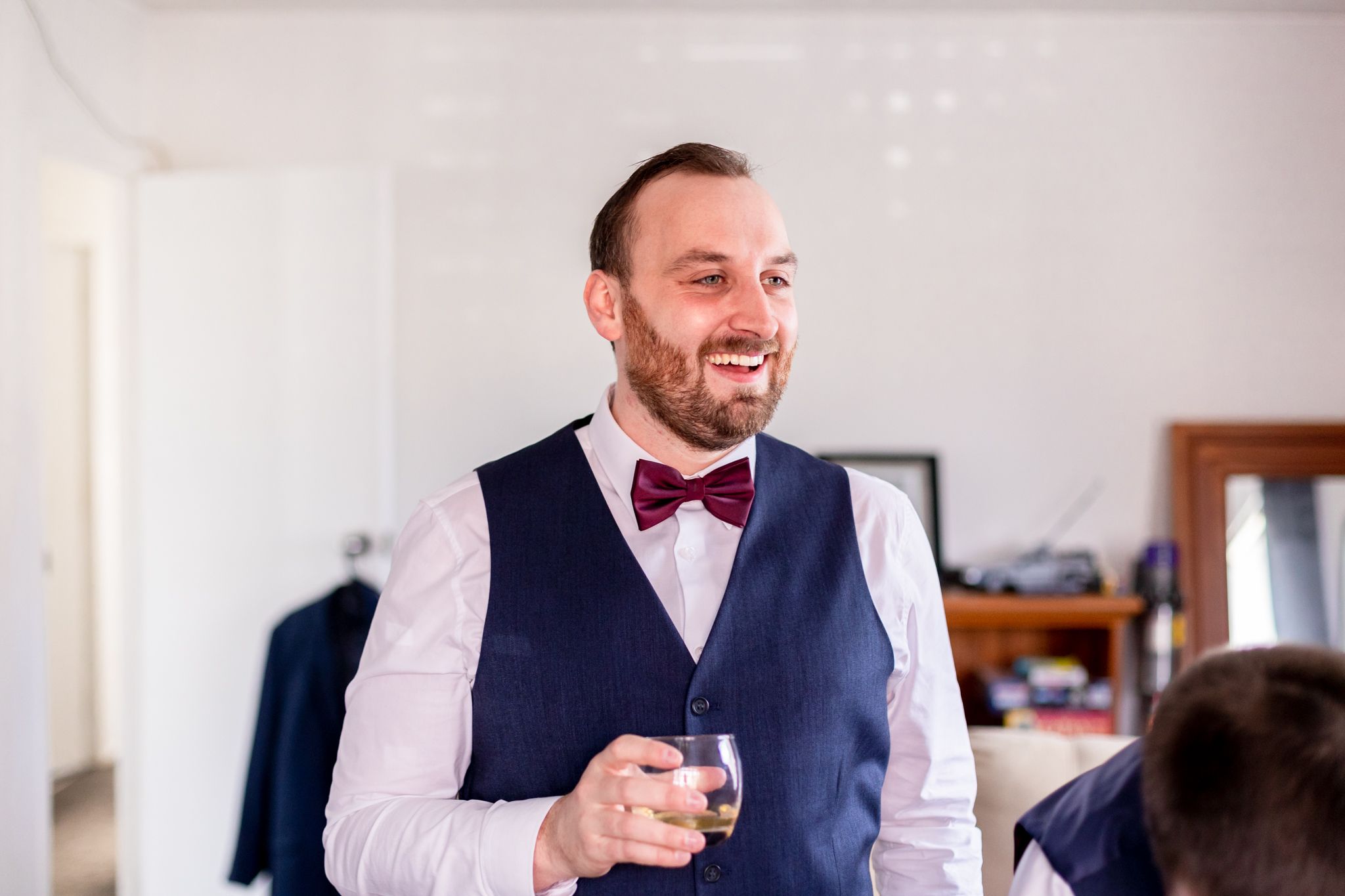 Groom in navy vest and bow tie smiling during wedding preparations.