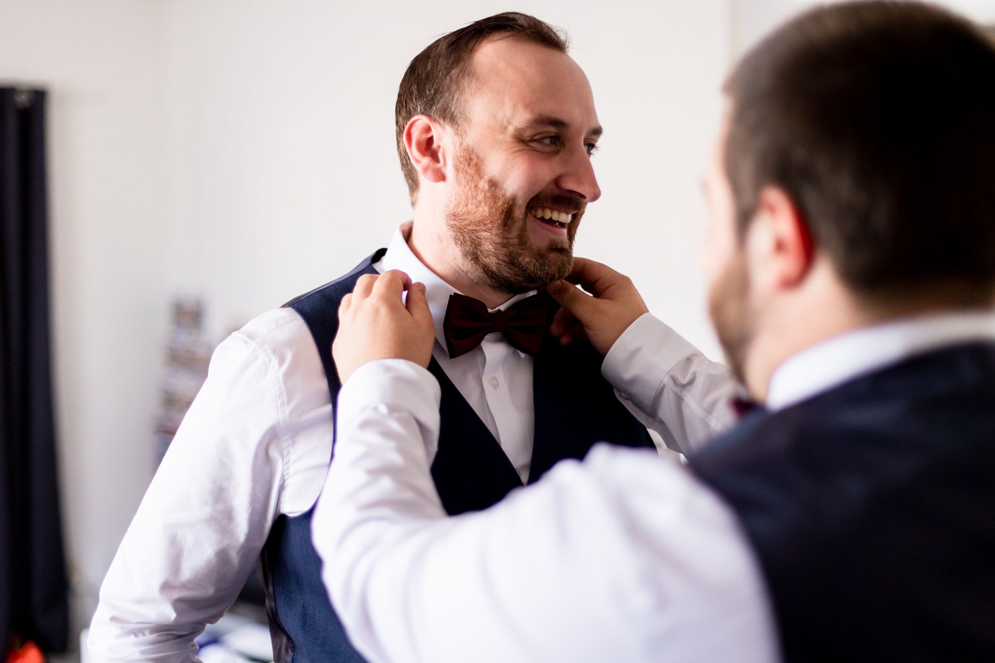 Wedding preparation scene with bow tie adjustment in formal attire.