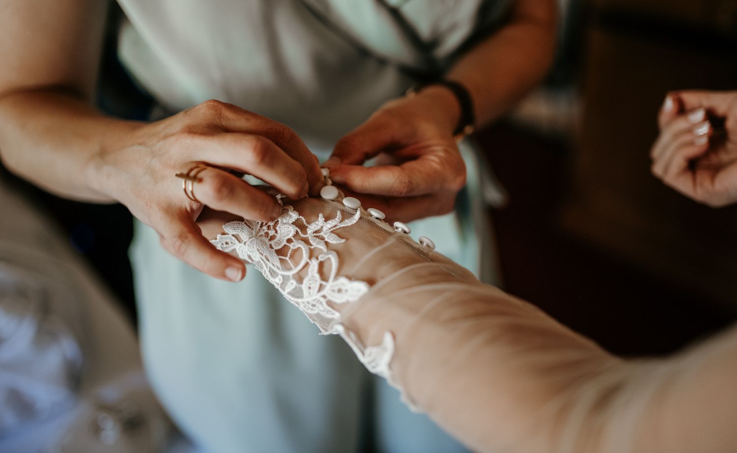 Close-up of hands fastening delicate lace bridal glove buttons during wedding day preparations.