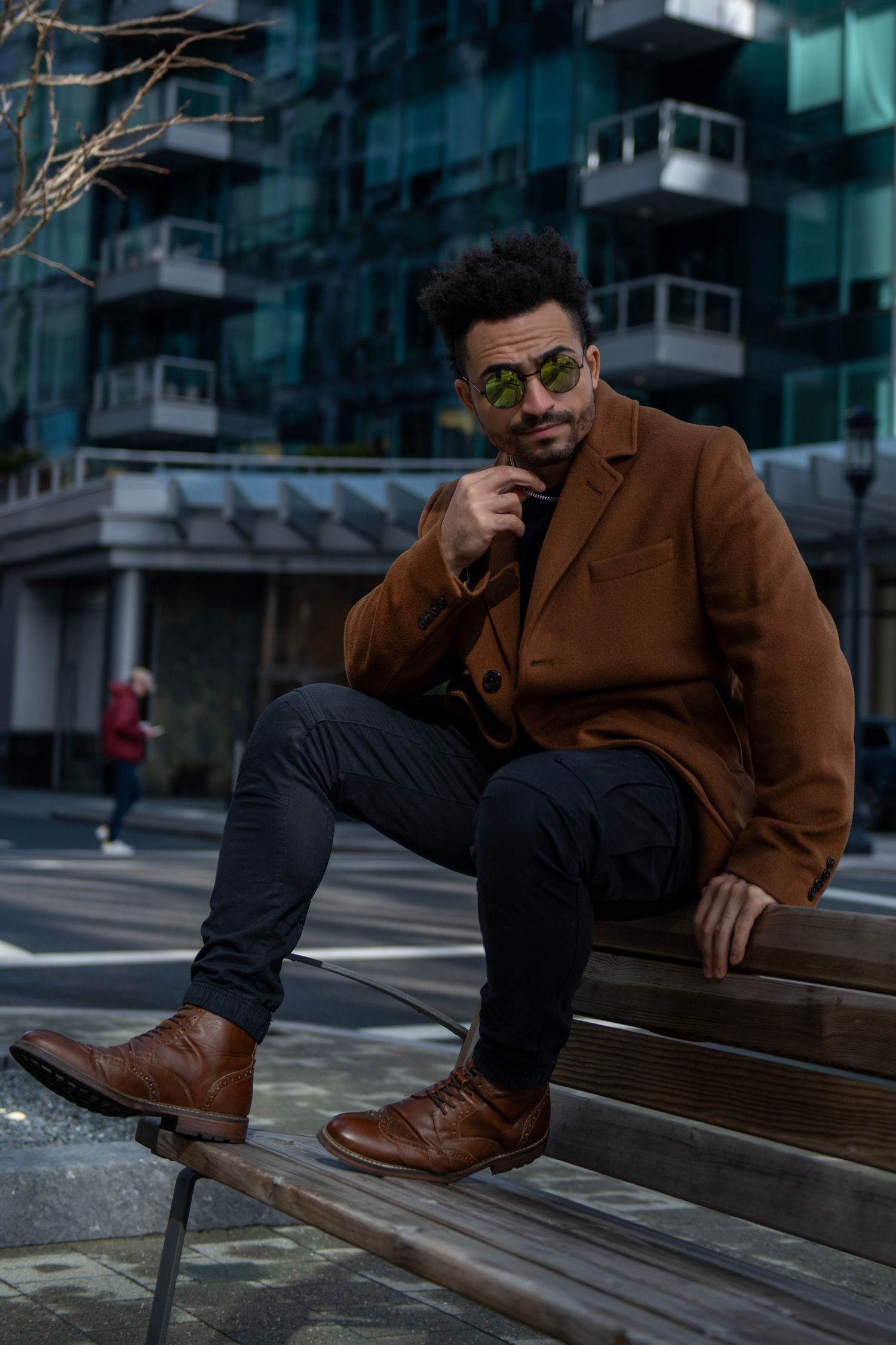 Stylish person in brown coat and boots poses thoughtfully on urban steps.