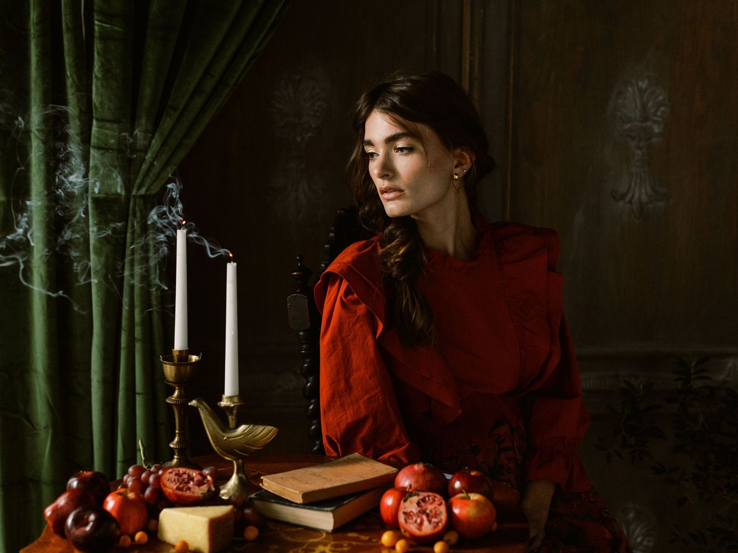 Still life with red dress, candles, pomegranates and green velvet curtain in dramatic lighting.