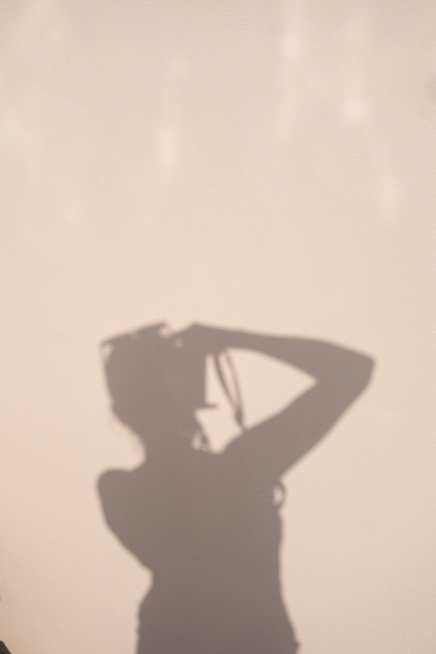 Shadow silhouette of person adjusting their hat against a plain light colored wall.