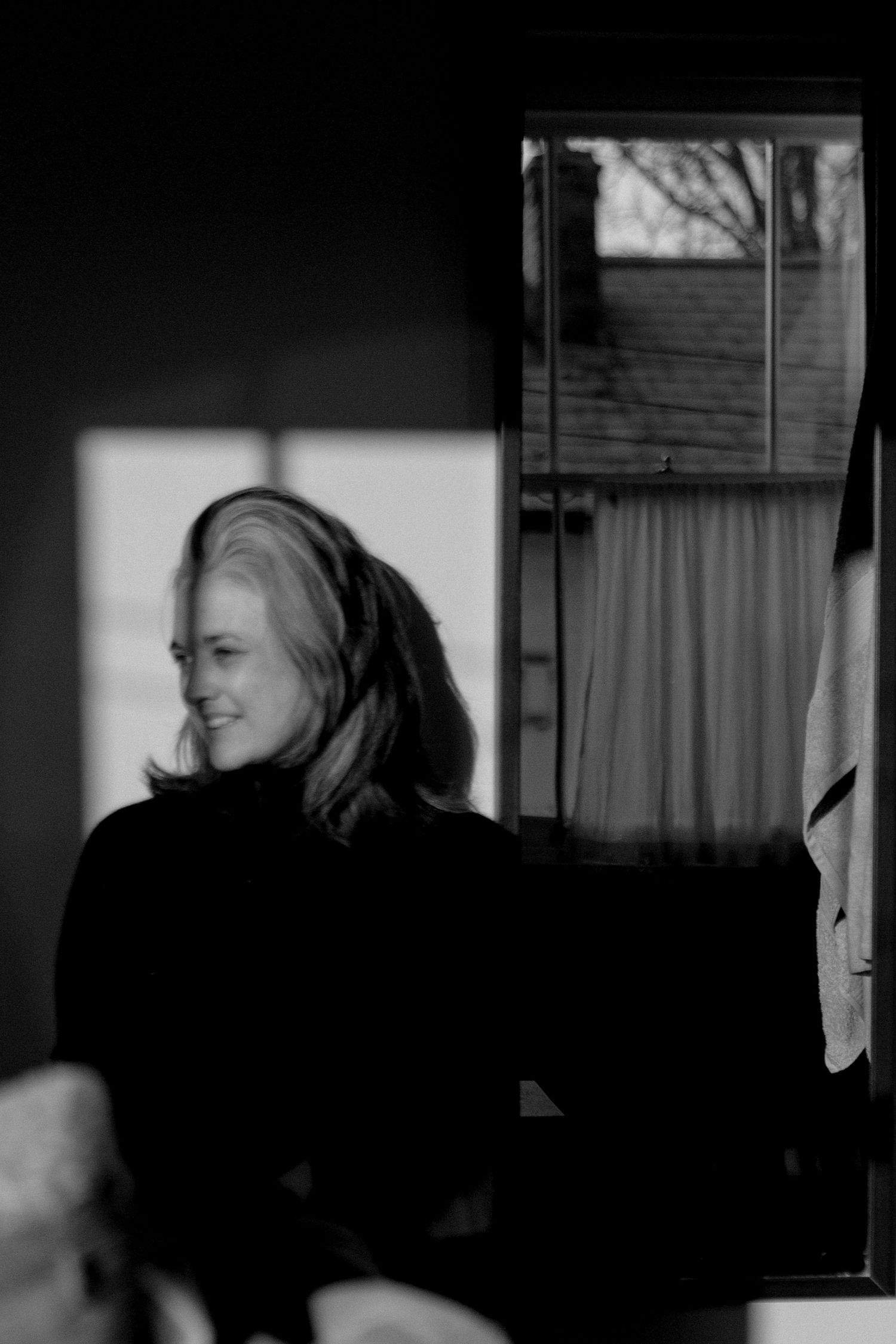 A black and white artistic portrait showing silhouetted figure in profile against soft window light and curtains.
