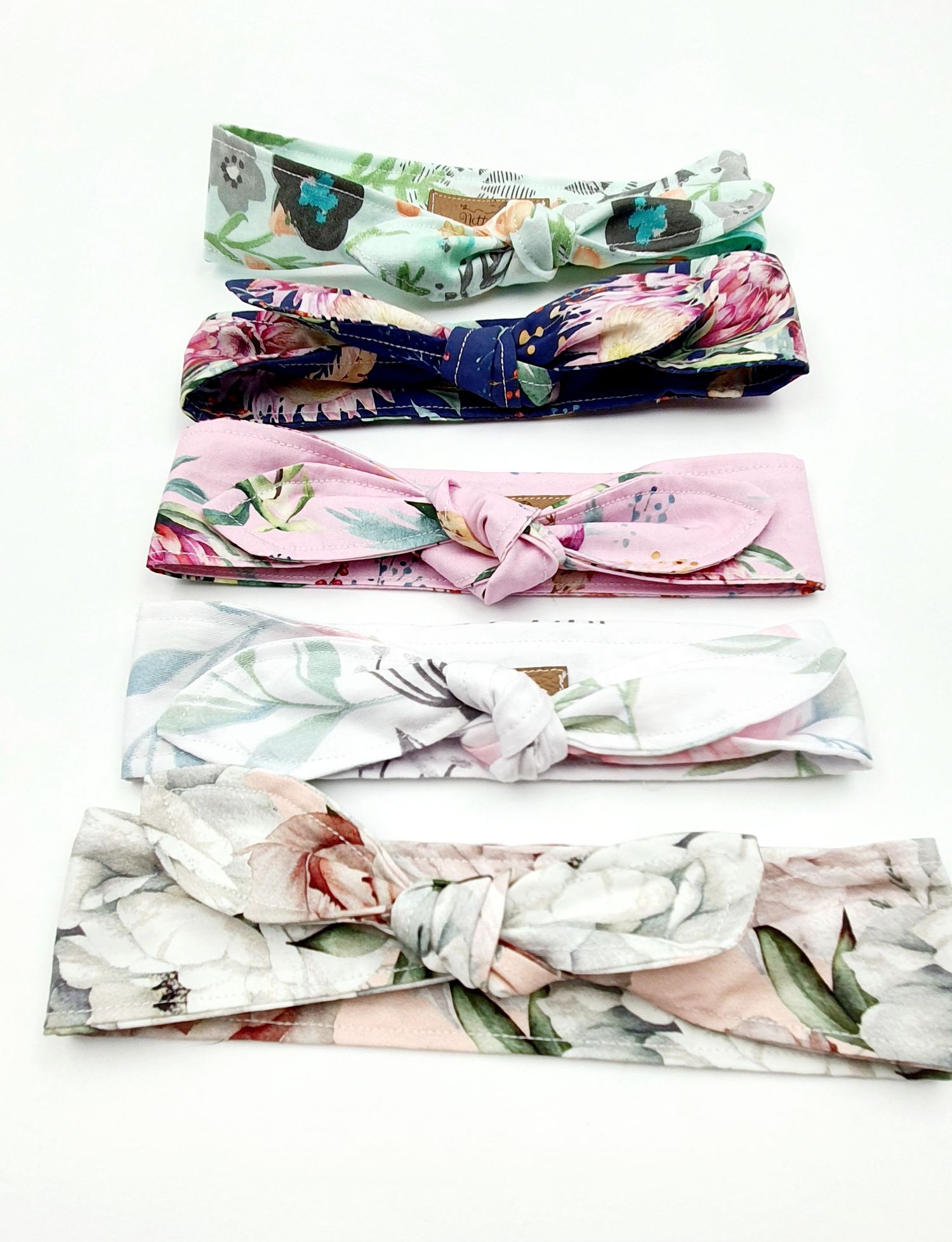 Five floral fabric headbands with knotted bow detail in pink, white, mint, and navy patterns on white background.