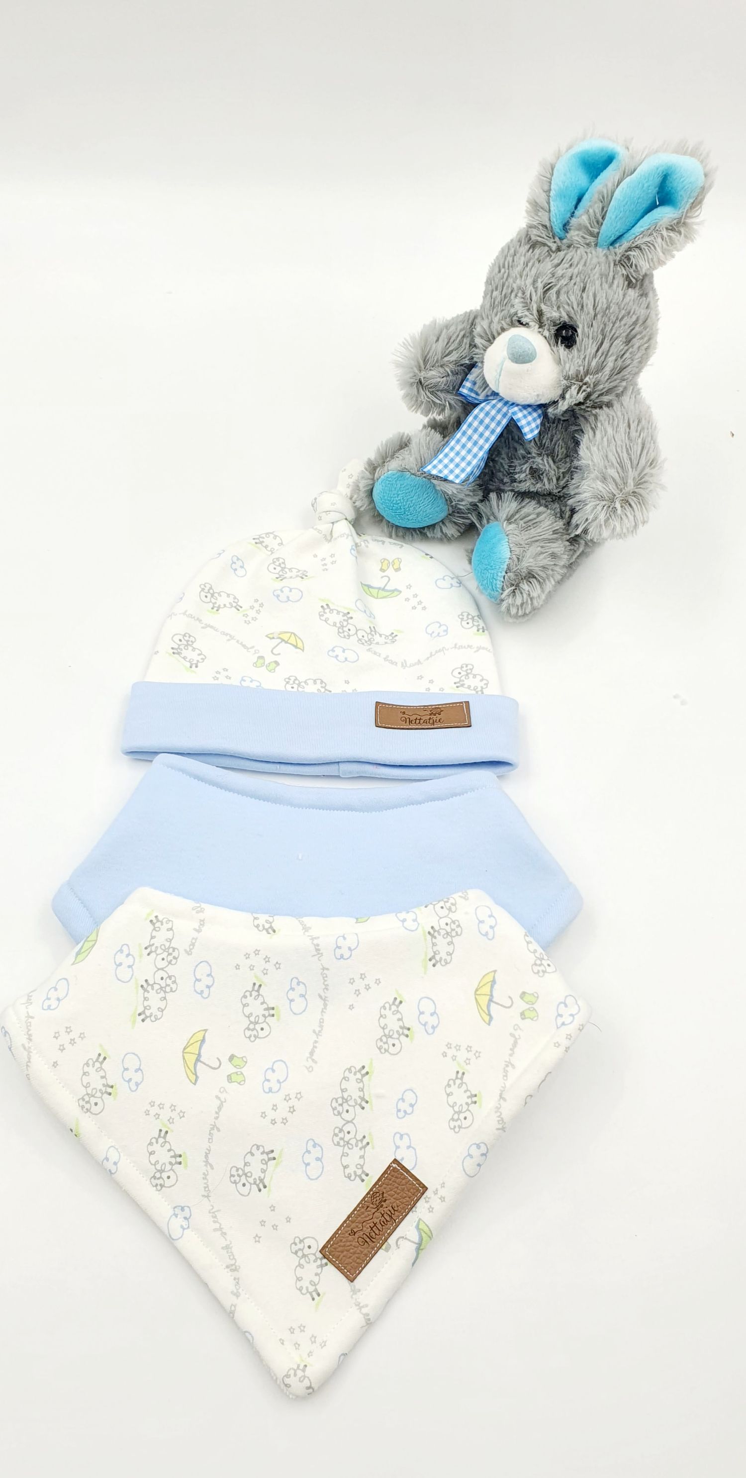 Baby blue floral hat and bandana bib set displayed with a gray plush bunny toy with blue bow tie.