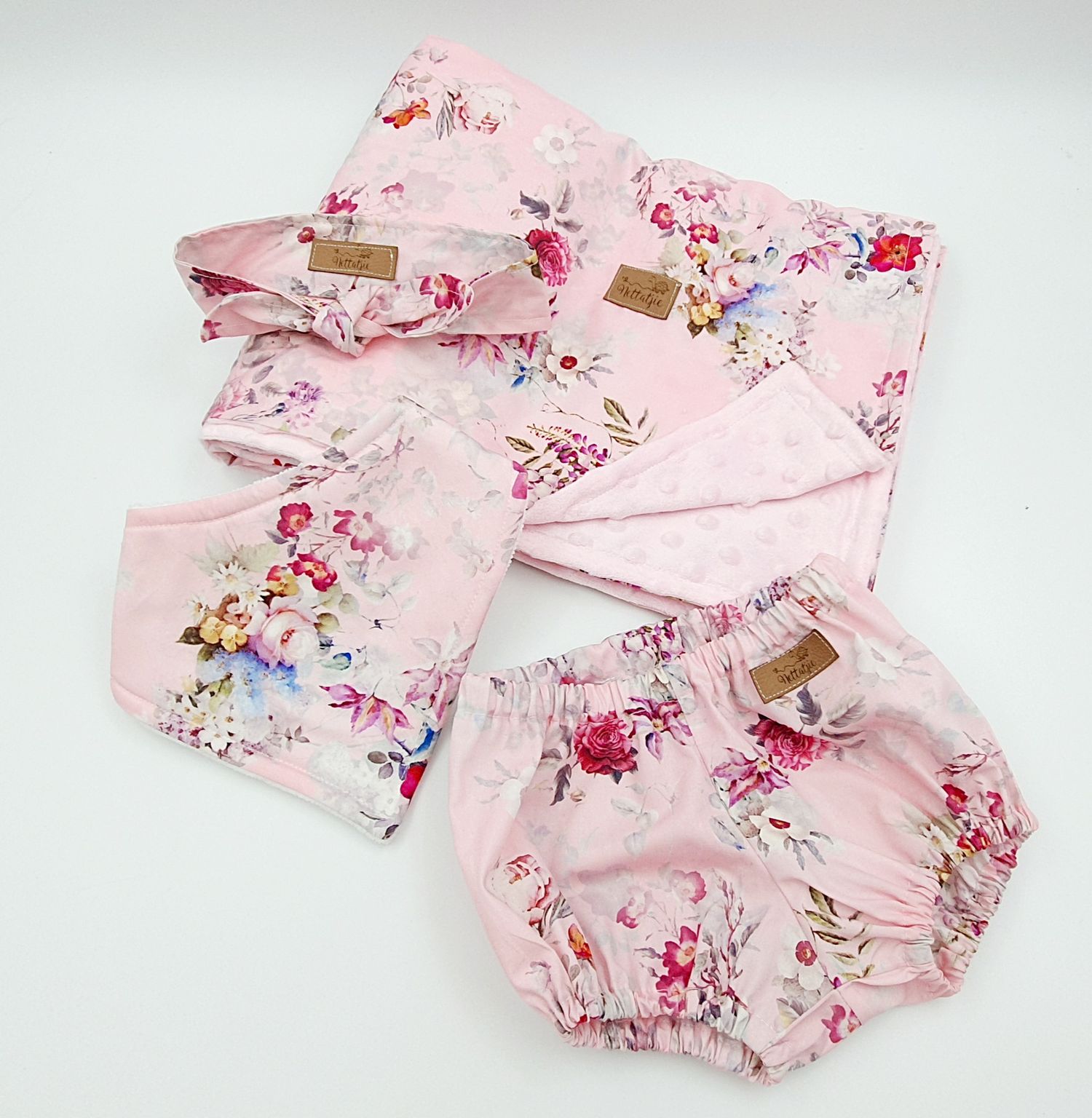 Pink floral baby girl set with bloomers, headband, bib, and blanket featuring rose print on soft fabric.