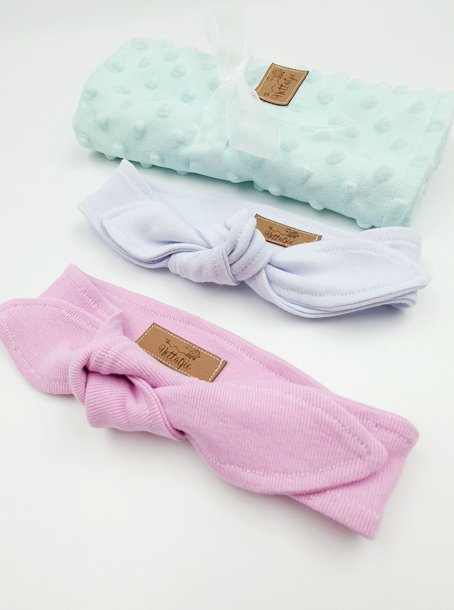 Three pastel hair headbands in mint, lavender, and pink with knotted bow details and branded leather labels.