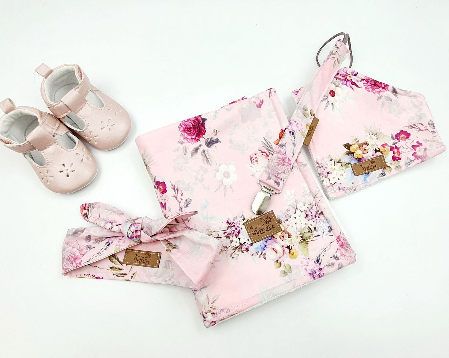 Pink floral baby girl set with swaddle blanket, headband, bib, and pink Mary Jane shoes on white background.