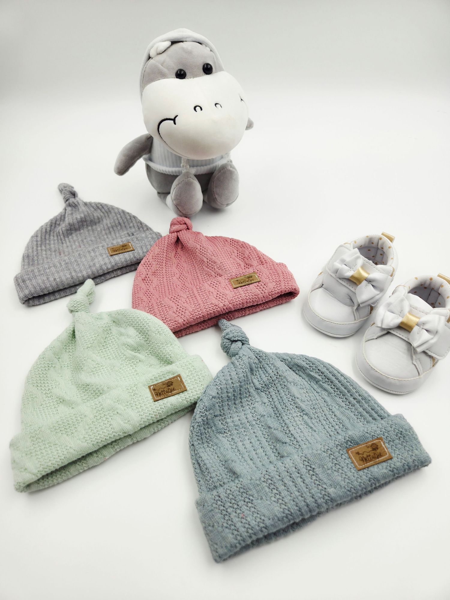 Baby accessories set featuring knit beanies, plush toys, and soft booties in pastel colors.