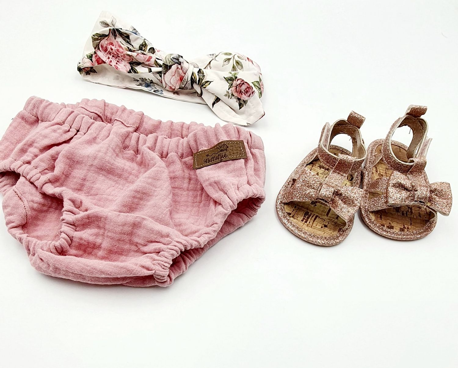 Pink muslin baby bloomer set with floral knotted headband and rose gold glitter bow sandals.