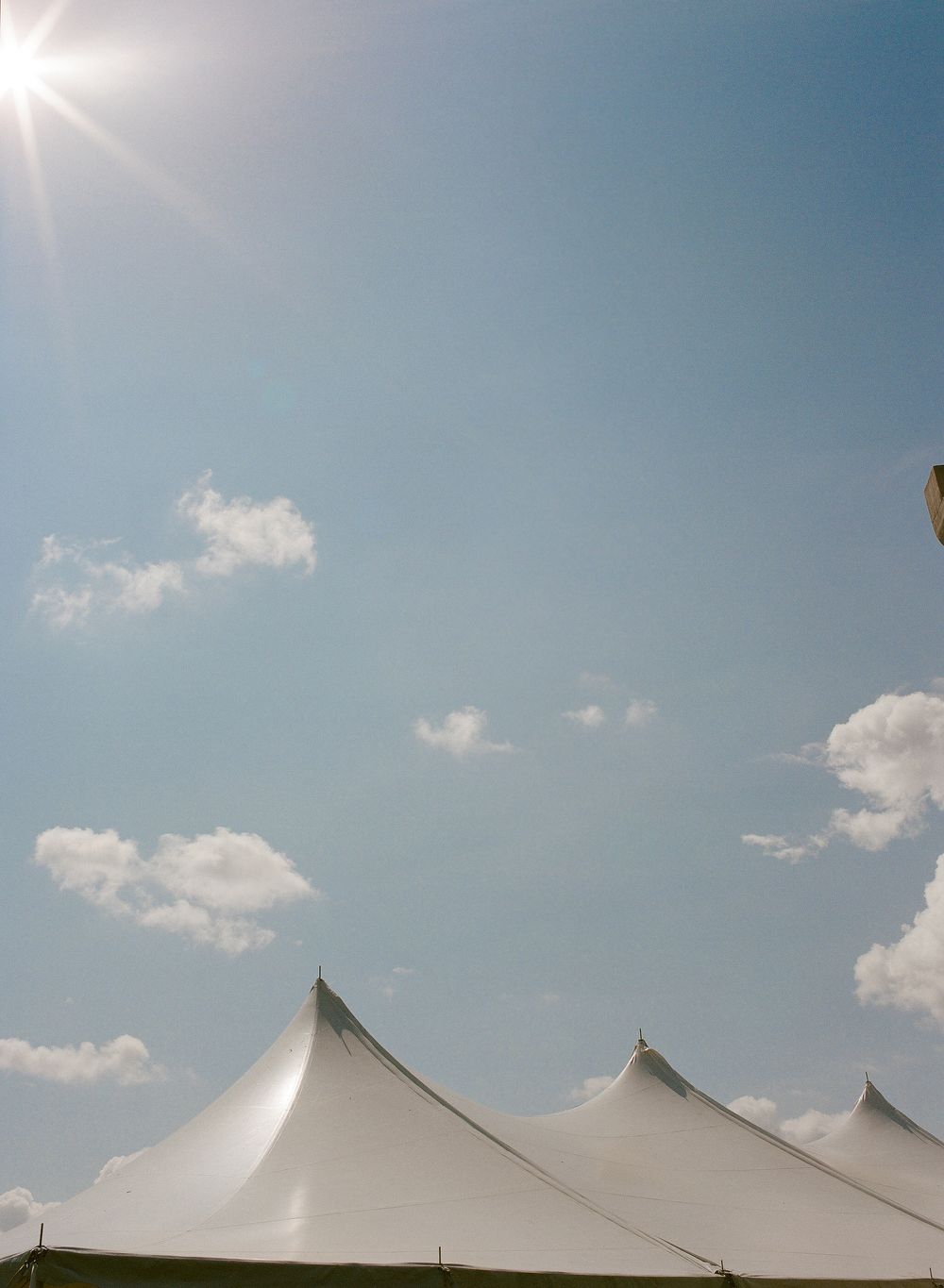White event tents gleam under bright summer sun against a blue sky with scattered clouds.