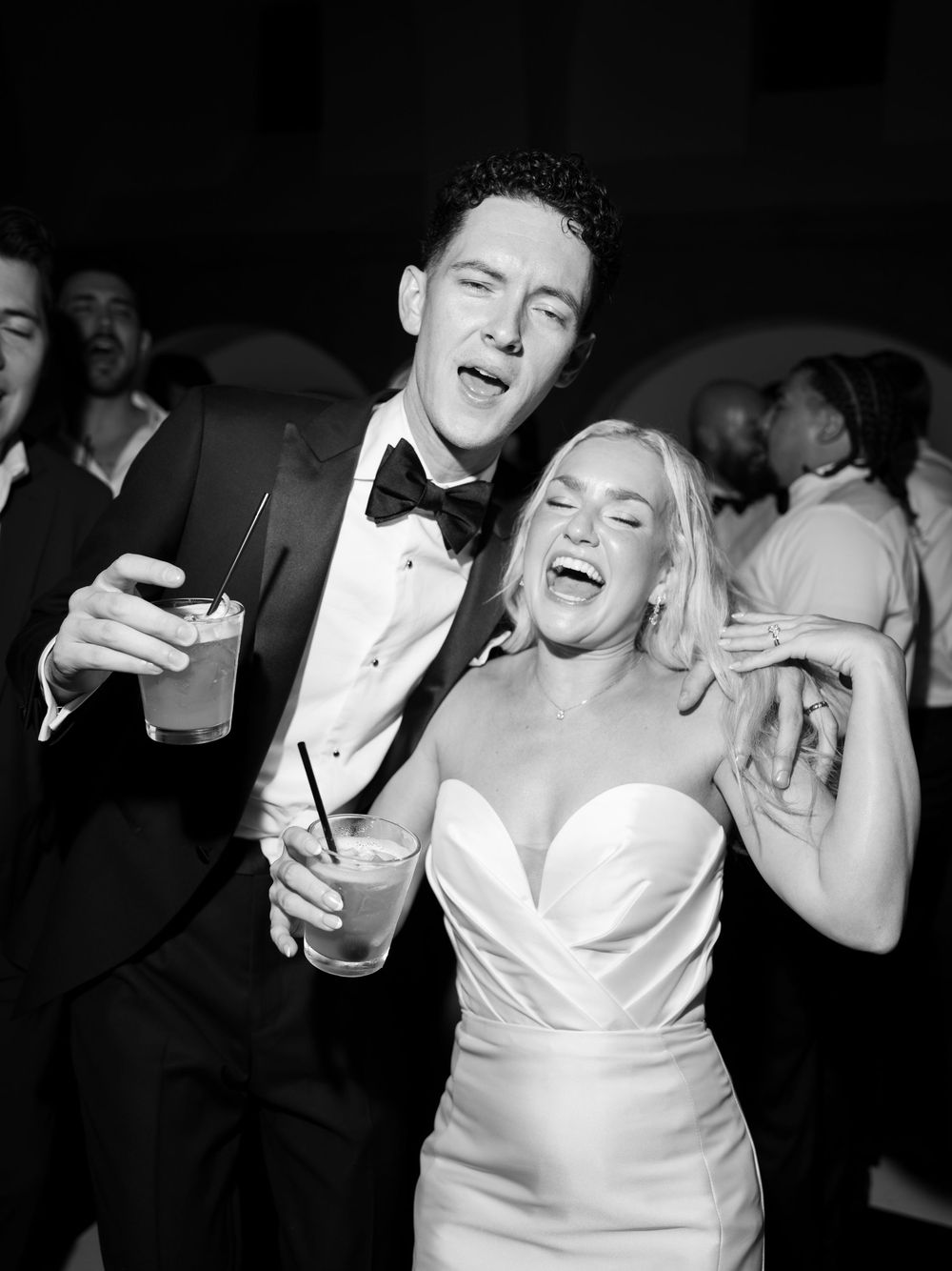Black and white photo of a joyful bride and groom dancing and laughing at their wedding reception.