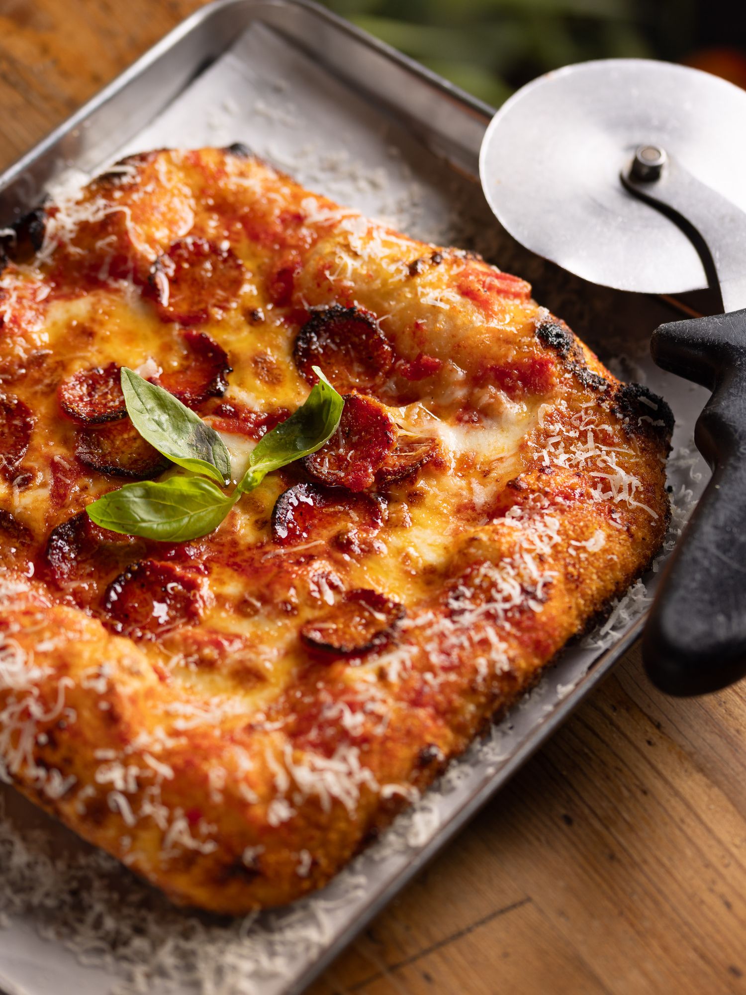 Pepperoni pizza with fresh basil and melted mozzarella on a rustic baking tray, Italian restaurant food photography at Made in Italy London