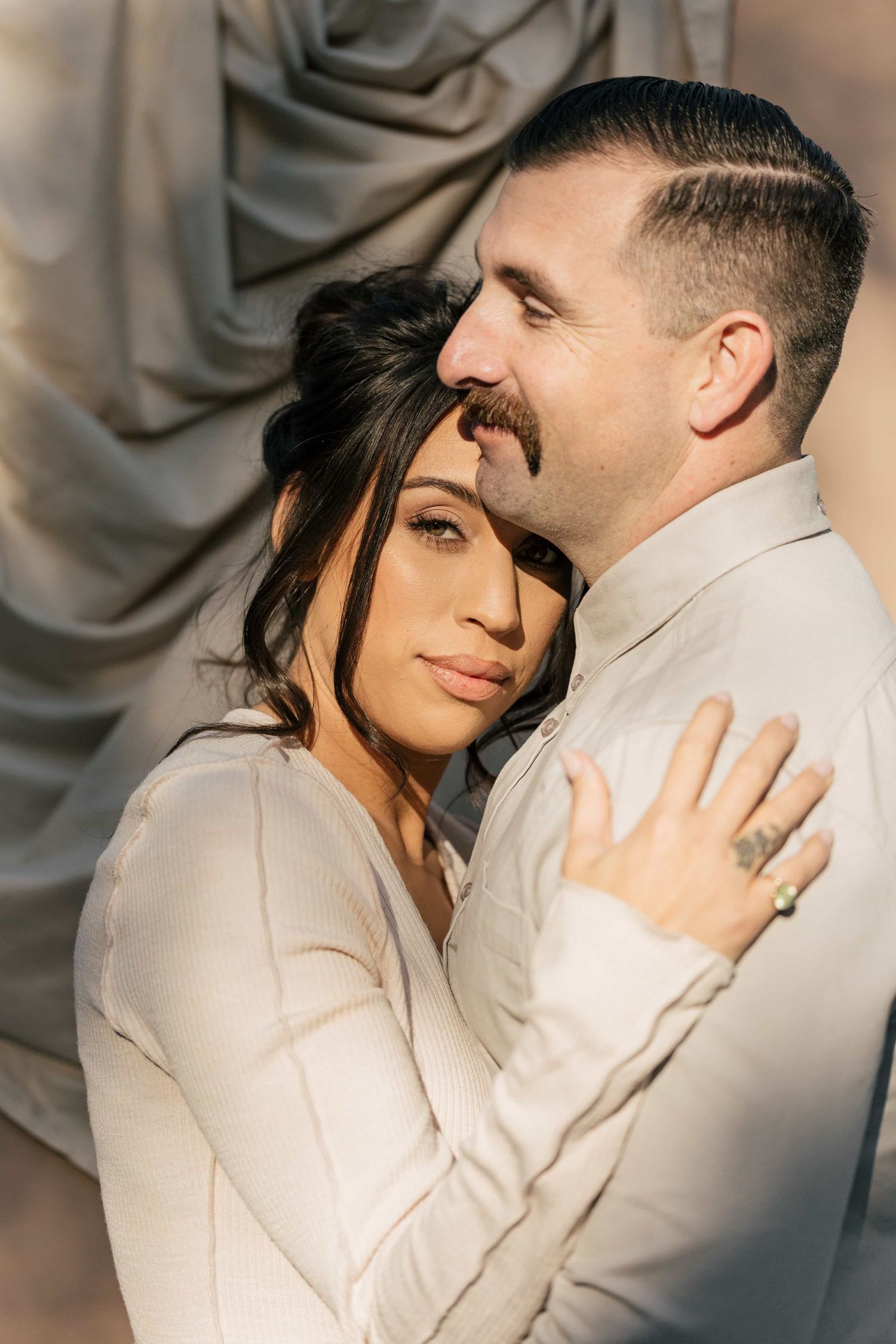 Couple in neutral tones embracing intimately, woman resting head on mans chest in elegant portrait.