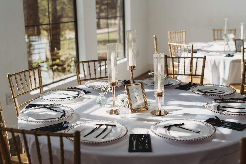 Elegant table settings with white linens and gold chiavari chairs in a bright banquet hall.