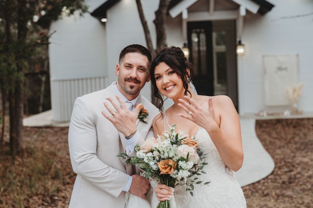 A wedding couple poses in a white outdoor setting with elegant floral arrangements and rustic decor.