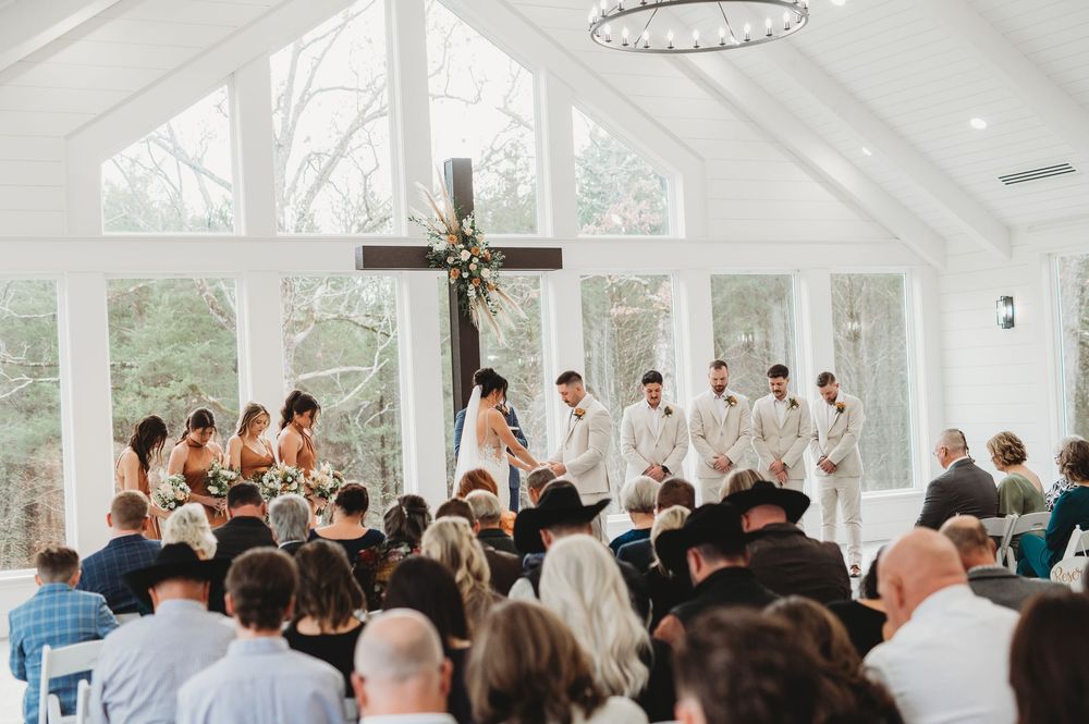 Wedding guests celebrate with raised arms in a bright white chapel with large windows and a wooden cross.