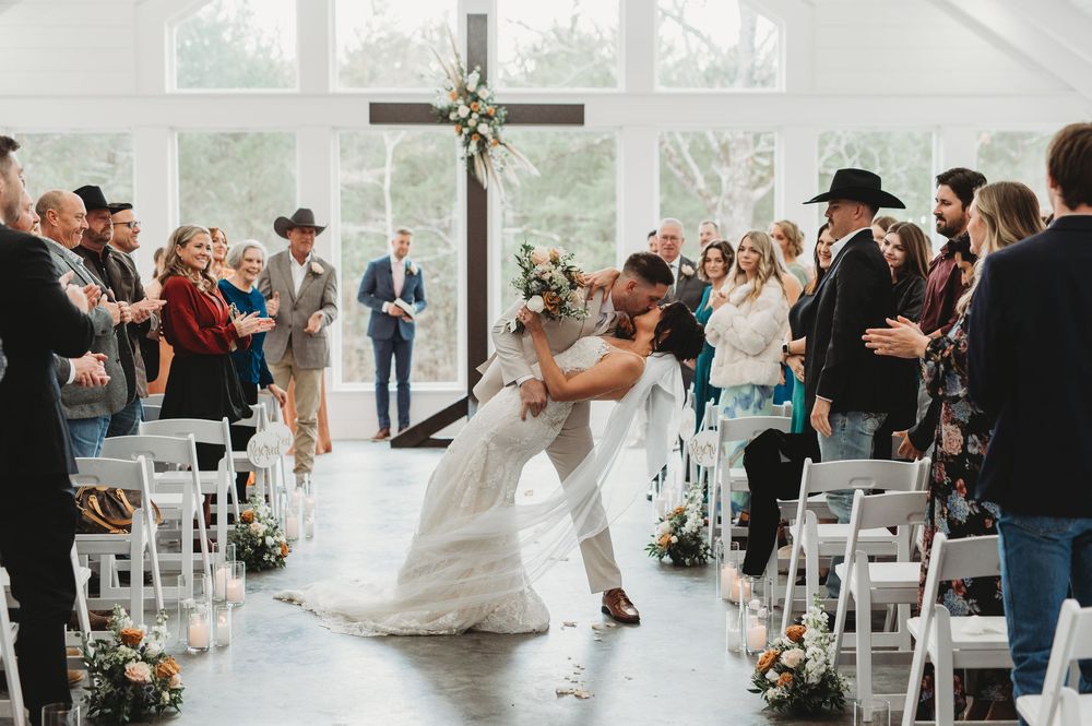Wedding ceremony panorama shows guests seated in white chairs inside a modern, light-filled chapel.