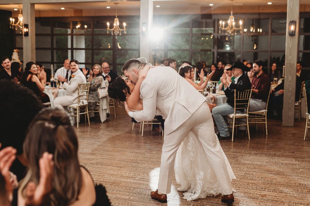 Wedding guests dance and celebrate on a rustic wooden dance floor at an elegant reception venue with chandeliers.