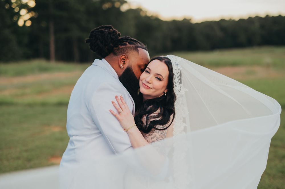 A romantic outdoor wedding photoshoot with a flowing white veil catching the breeze in a grassy field.