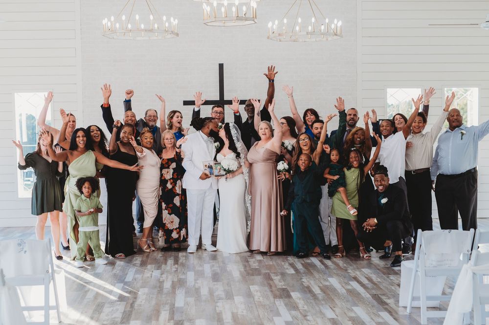Wedding guests celebrate with raised arms in a bright white modern venue during a joyful reception moment.