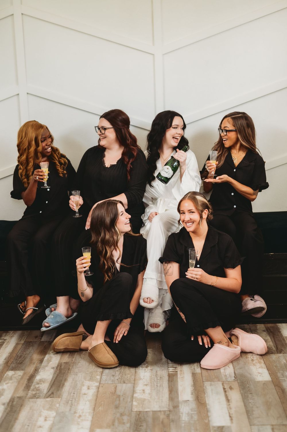 A group of women in black outfits sitting on a wooden floor in a sequence of candid photos showing laughter and friendship.