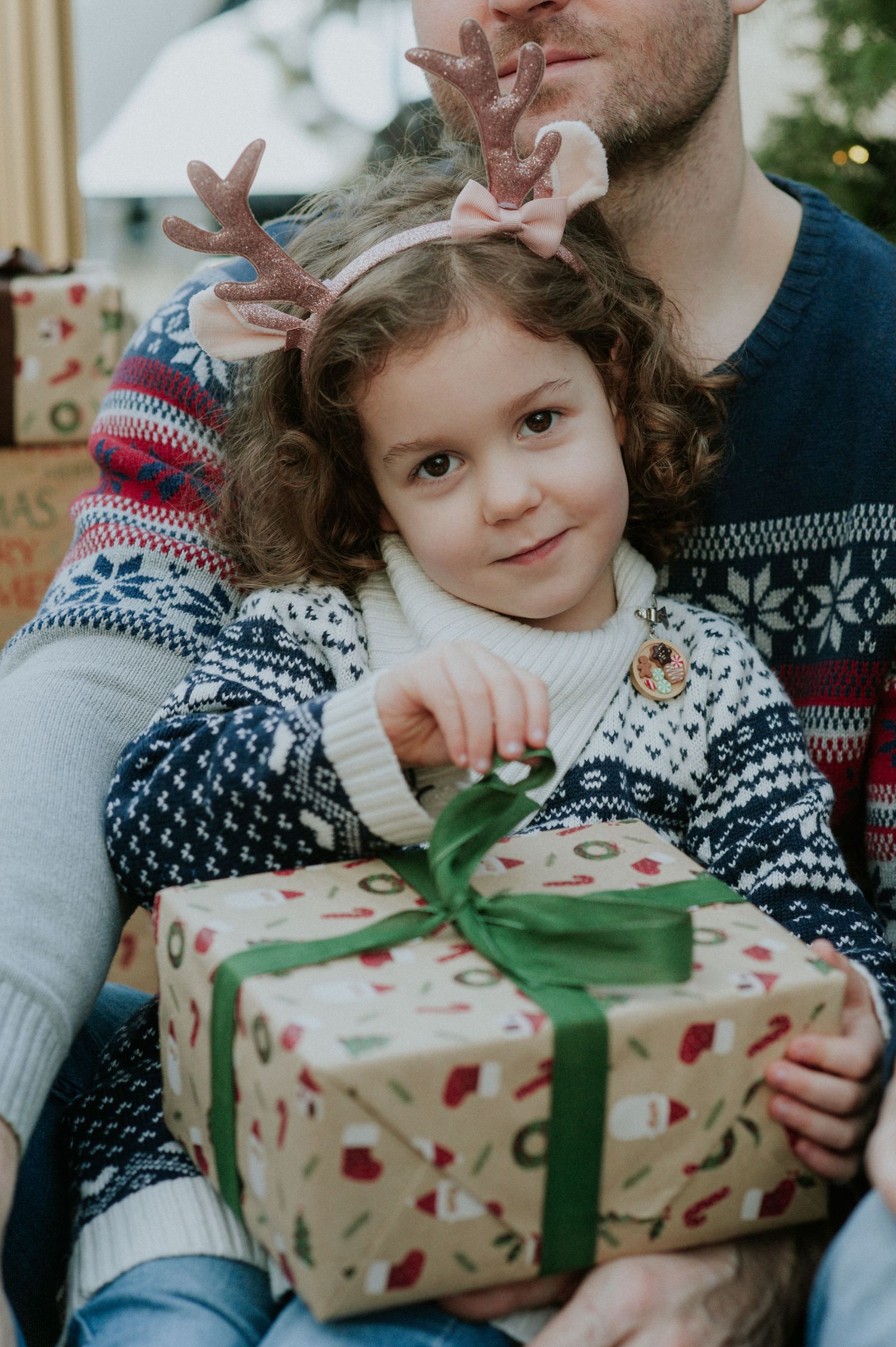 Joyful holiday moment opening a gift wrapped in santa print paper with a green ribbon.