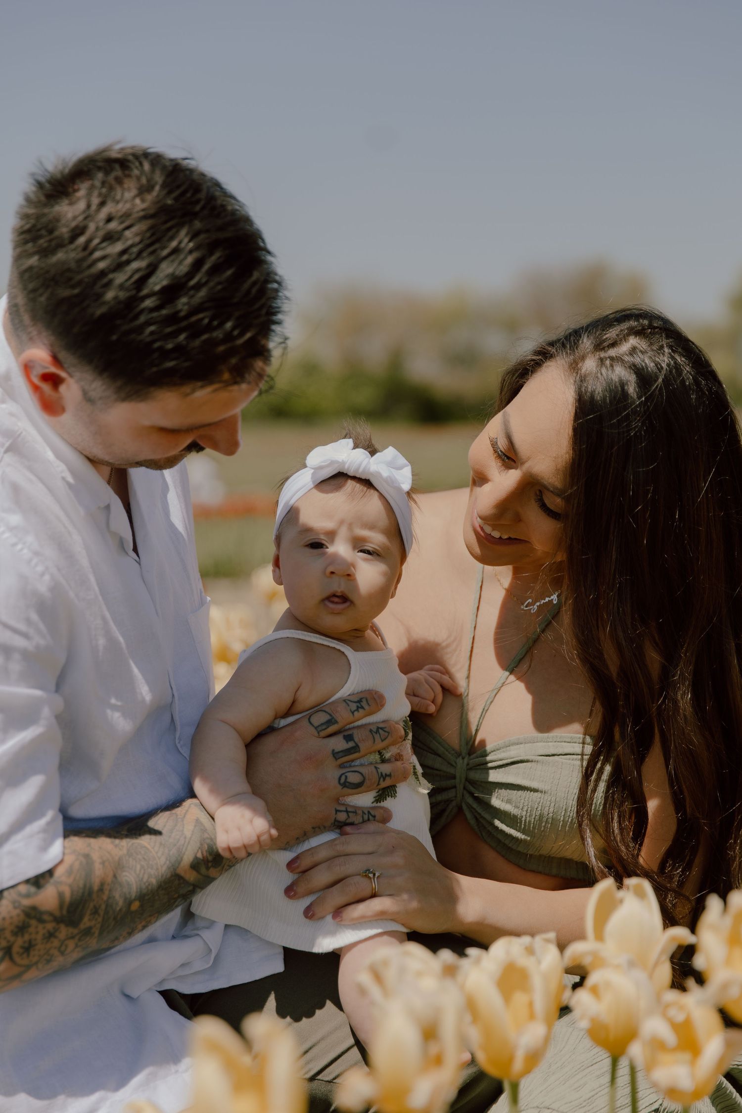 Family shares tender moments together while sitting in a springtime field of yellow tulips on a bright sunny day.