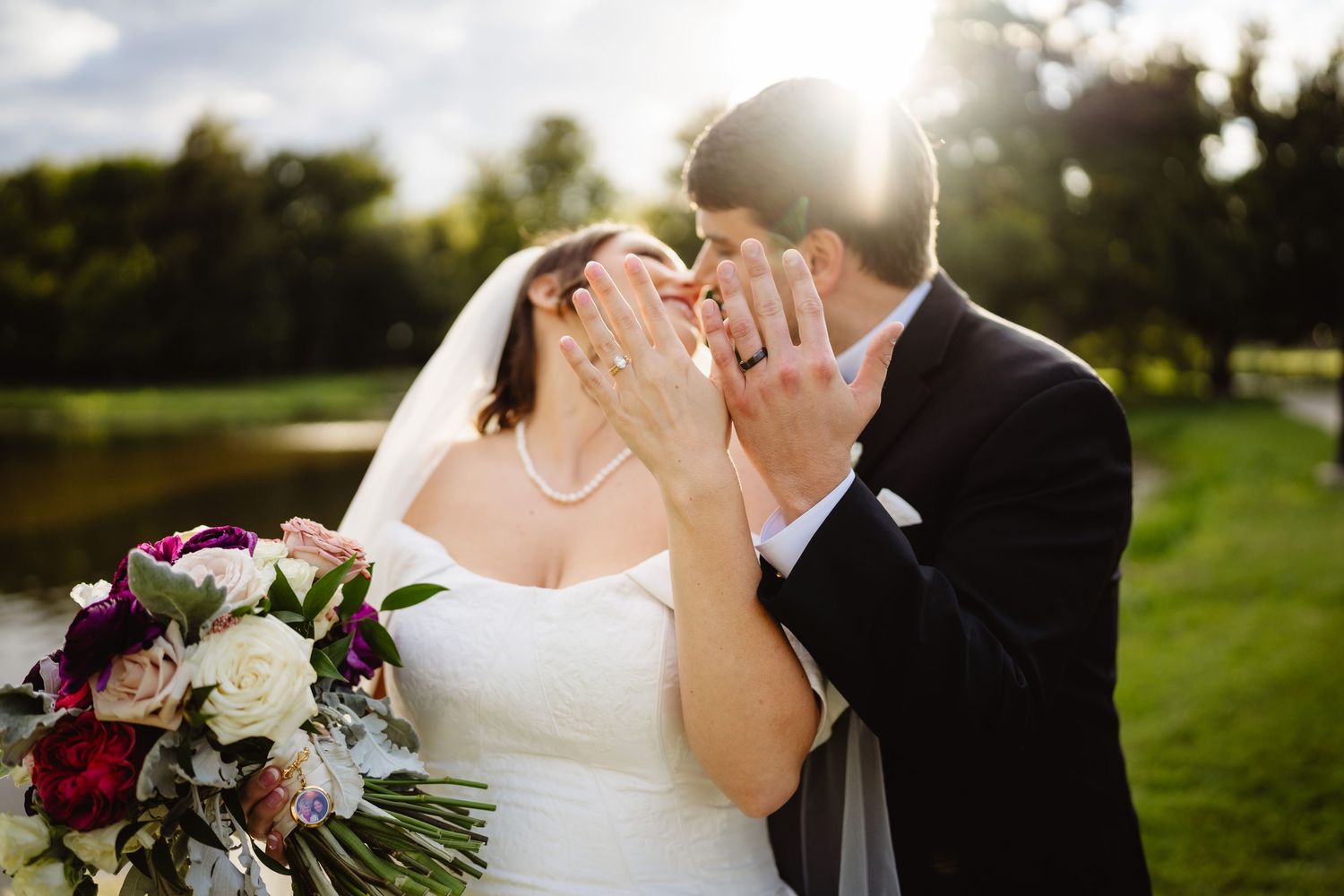 Wedding couple shares an intimate moment on a sunny golf course while holding a burgundy and white floral bouquet.