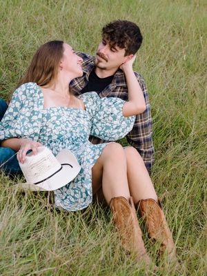 A romantic couple relaxes together in a grassy meadow on a sunny afternoon wearing casual attire and boots.