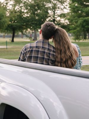 Close-up shot of someone leaning against the side of a white car at sunset.