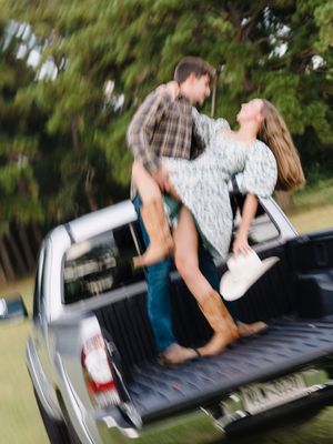 Two people playfully wrestling and falling into the back of a white pickup truck in a park setting.