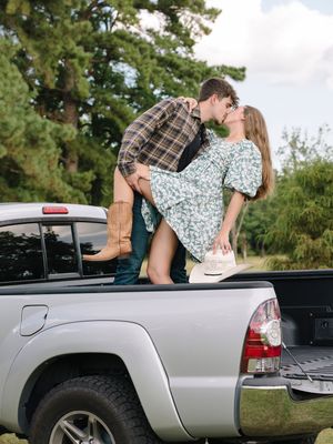 Romantic moment captured on pickup truck tailgate with countryside backdrop.