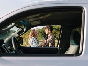View through car window of couple in casual western wear talking.