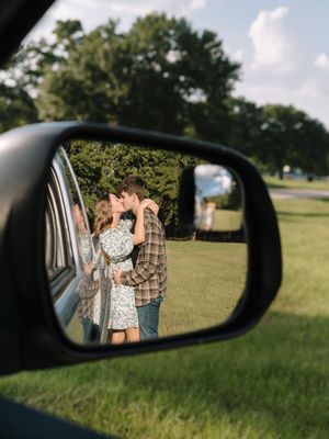 Side mirror reflection captures a couple sharing a romantic moment in a grassy field.