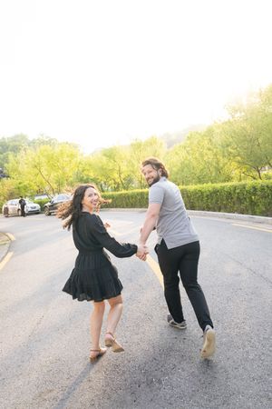 A playful couple dances together on a sunlit road in matching outfits.