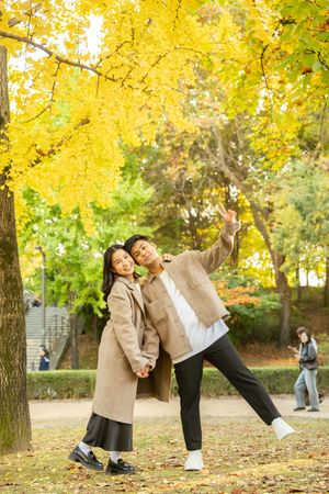 Two people pose creatively under yellow autumn trees in a park.