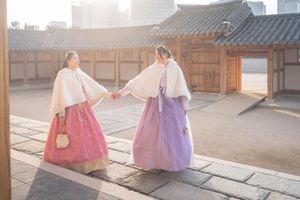 People wearing traditional Korean hanbok dresses walking along a temple courtyard.