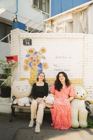 Two people sit on white decorative benches against a painted brick wall.