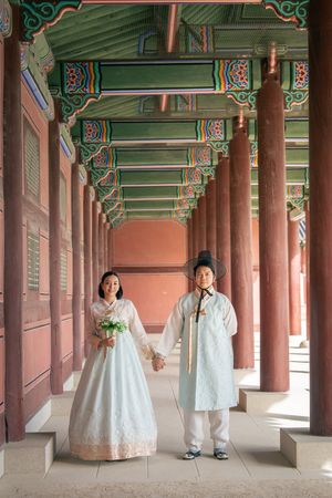 Traditional Korean wedding photo session in a palace courtyard with ornate wooden pillars and painted decorative details.