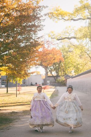 People wearing traditional Korean hanbok dresses pose in a park with autumn foliage in the background.