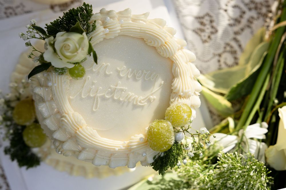 A white wedding cake decorated with fresh green and white flowers sits elegantly on display at a reception.